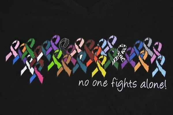 A black tee printed with colorful awareness ribbons and the words: no one fights alone