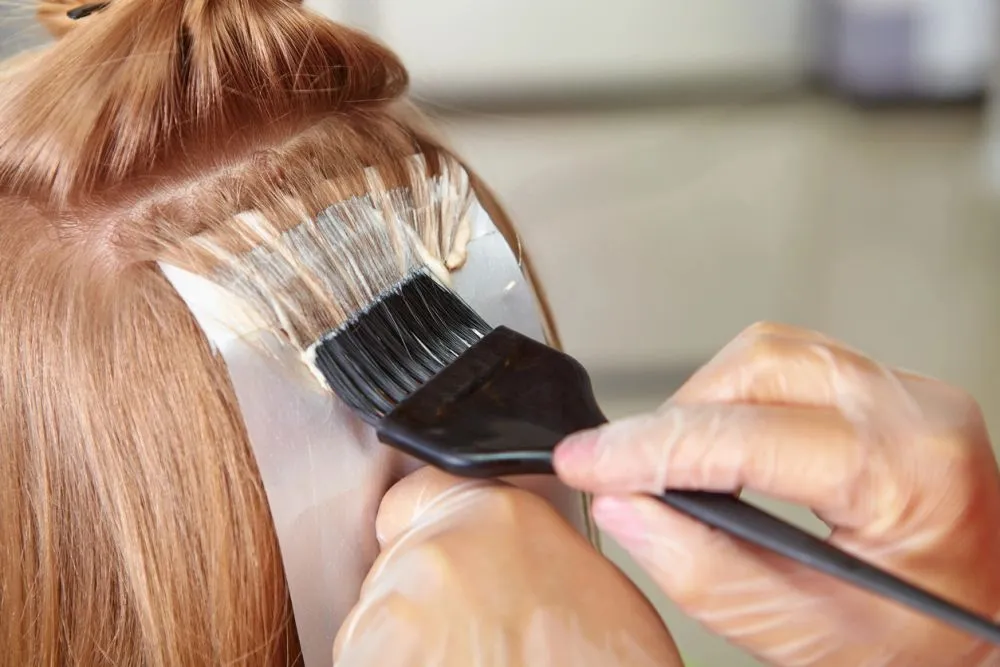 A colorist brushing lightener onto a guest's hair over a foil